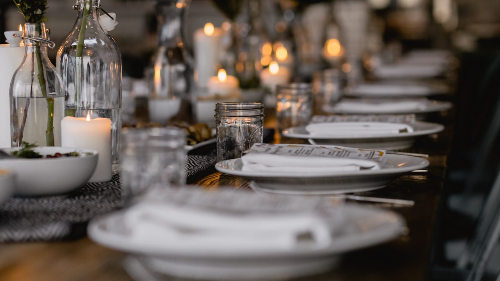 A long row of fancy table settings and a table centerpiece of softly glowing candles