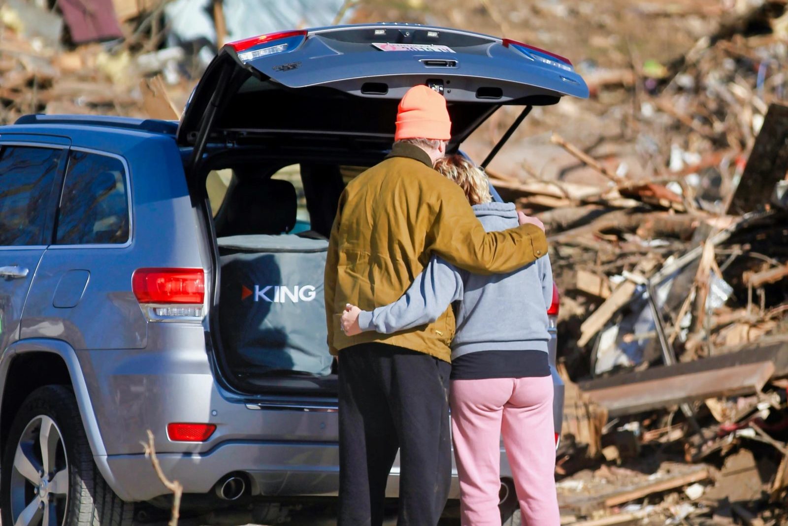 A man and woman hold each by a car amidst wreckage and rubble