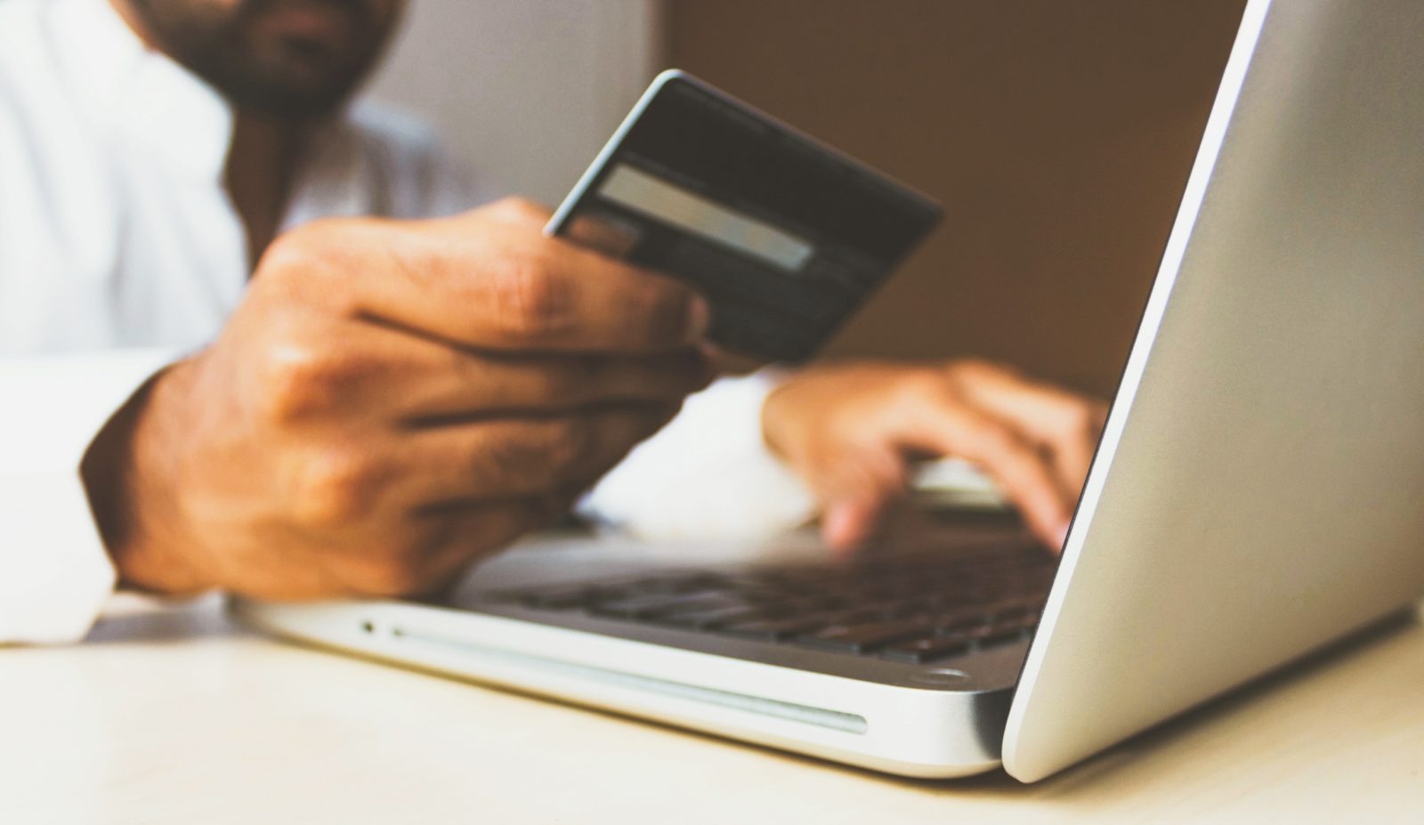 A man holds a credit card in his hand as he types the card's information into his MacBook laptop.