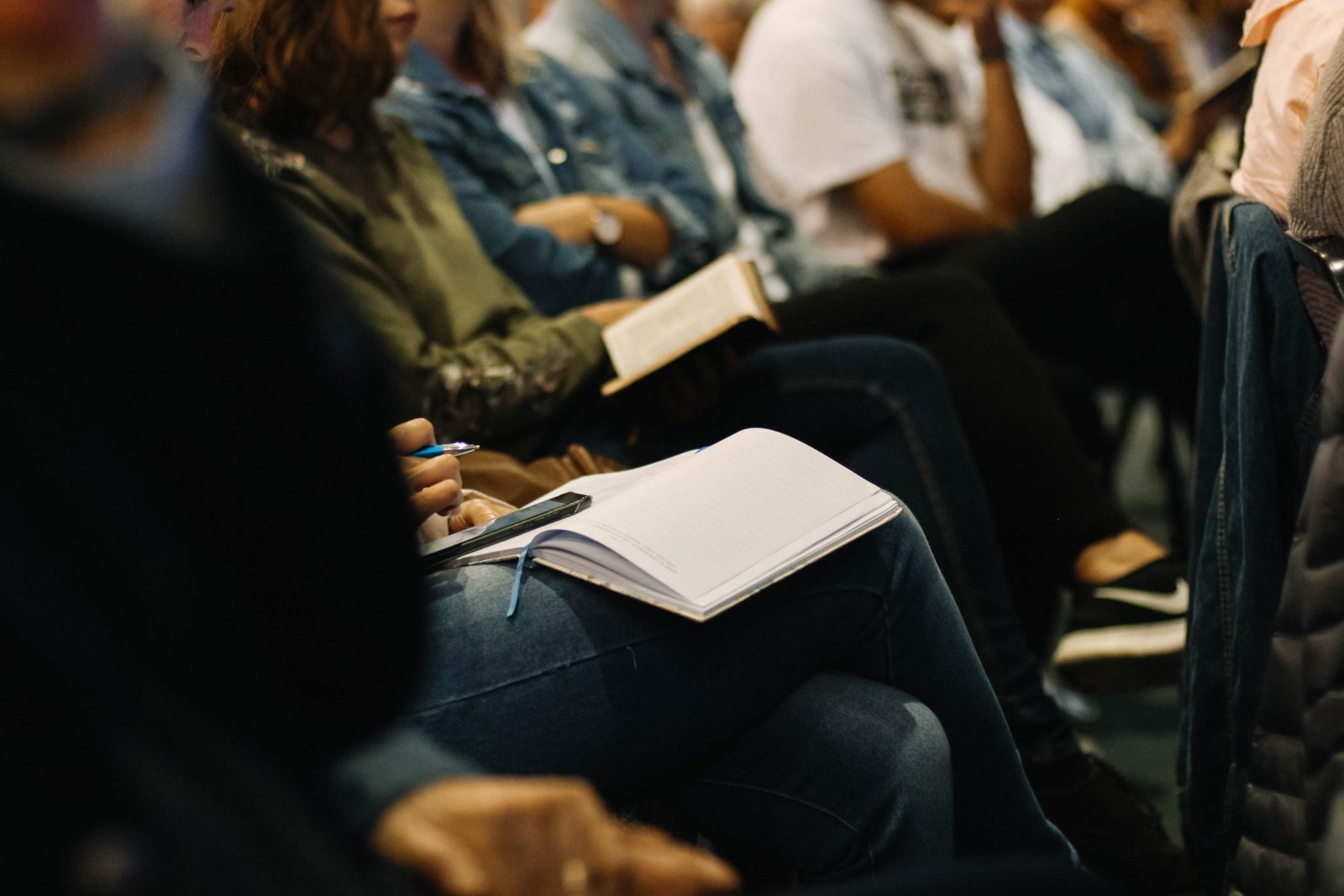 a woman attending a conference presentation with an open notebook in her lap.