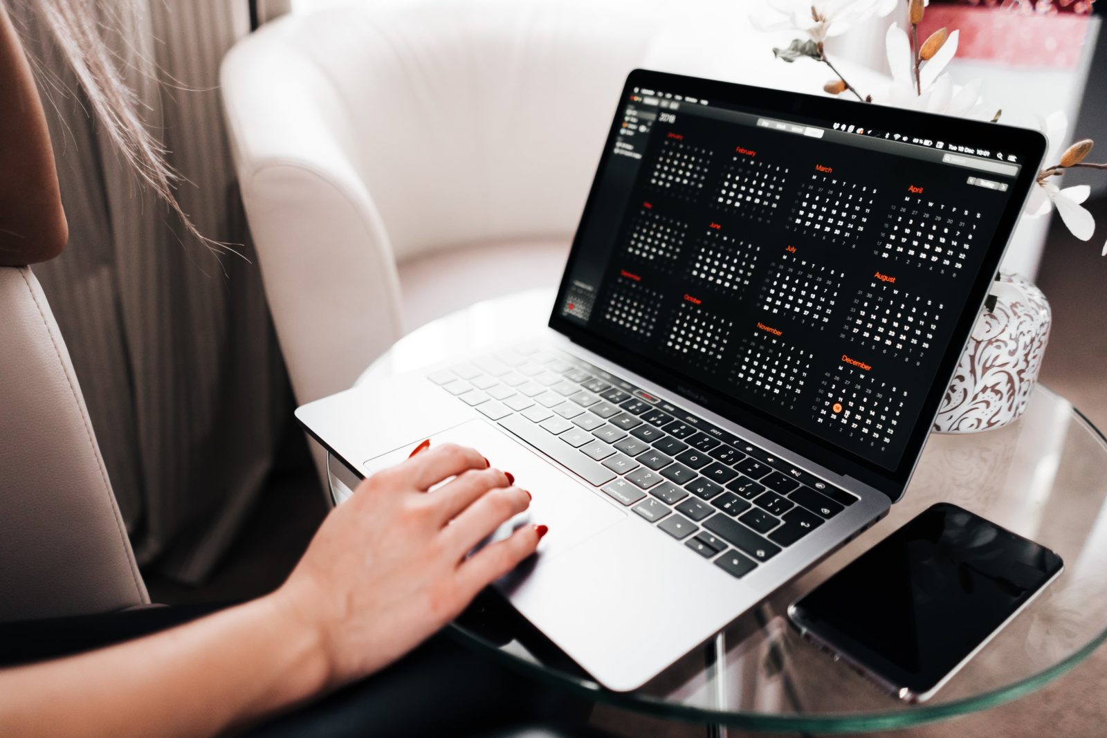 A good content calendar app will help you manage your channels and communicate consistently. A woman is working on a laptop, which displays a calendar