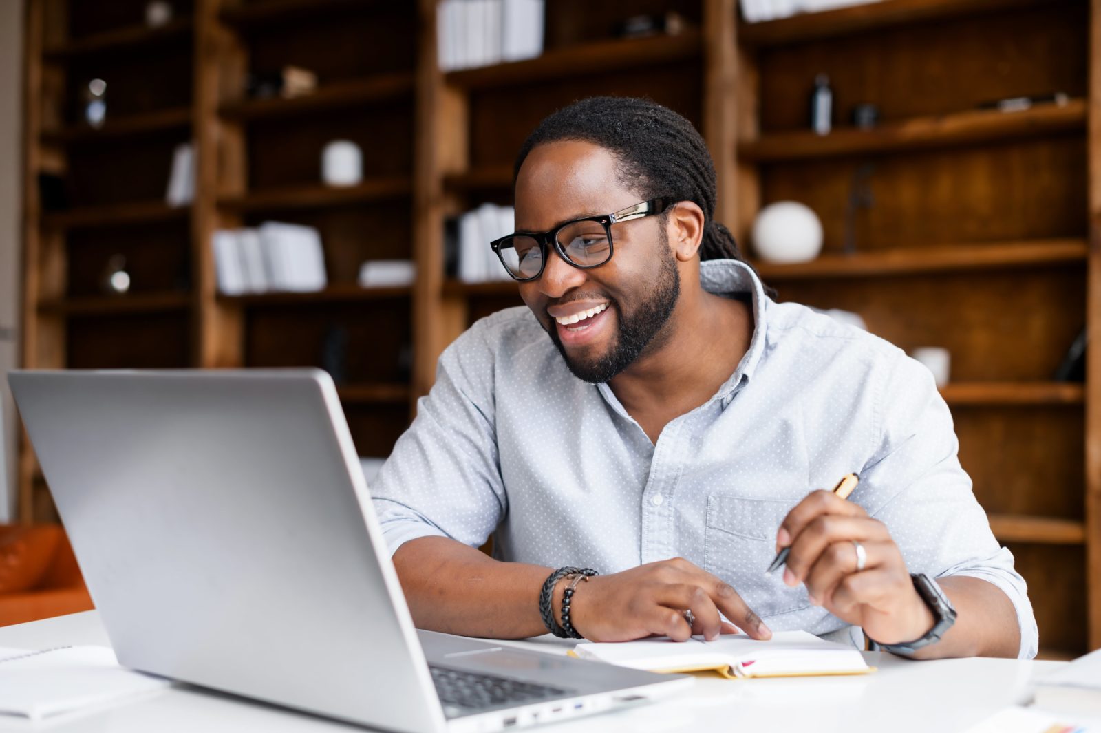 This image depicts a smiling man with long dark hair smiling at his laptop—choosing a nonprofit CRM may be a big decision for him, but this guide is making it a little easier