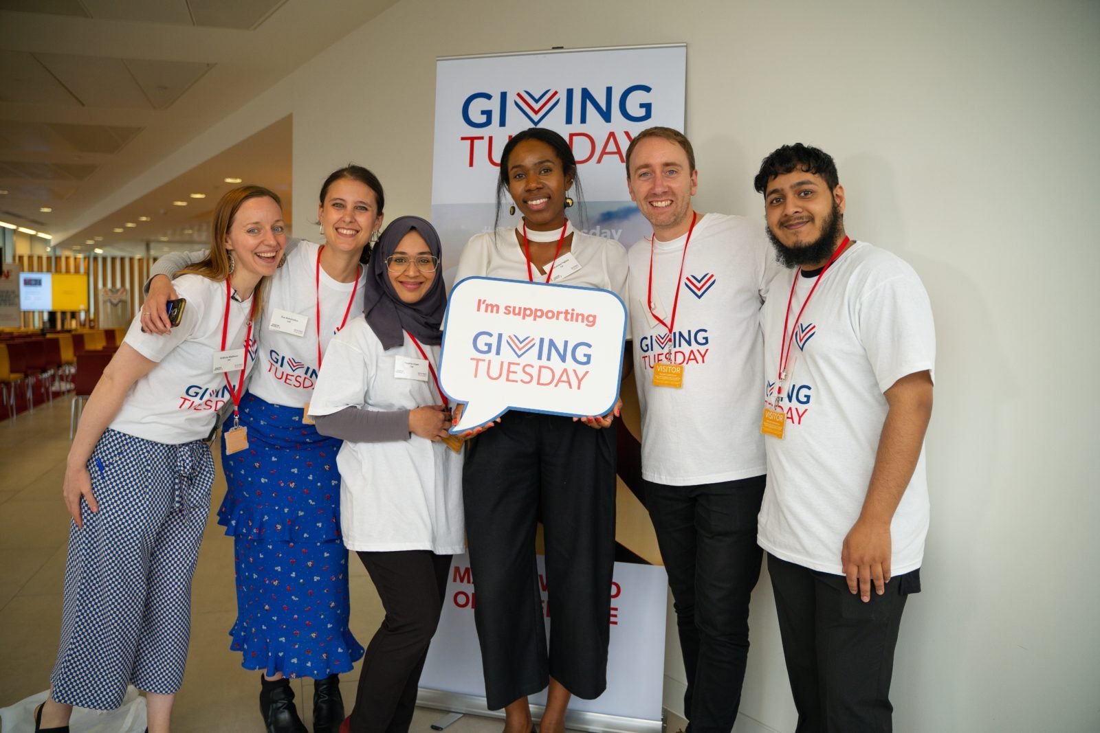 Six smiling students huddle together holding a small Giving Tuesday 2022 sign