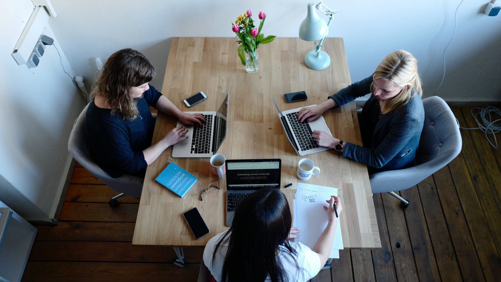 three women sitting around a table, working on their laptops, trying to figure out the best crm for their small nonprofit.
