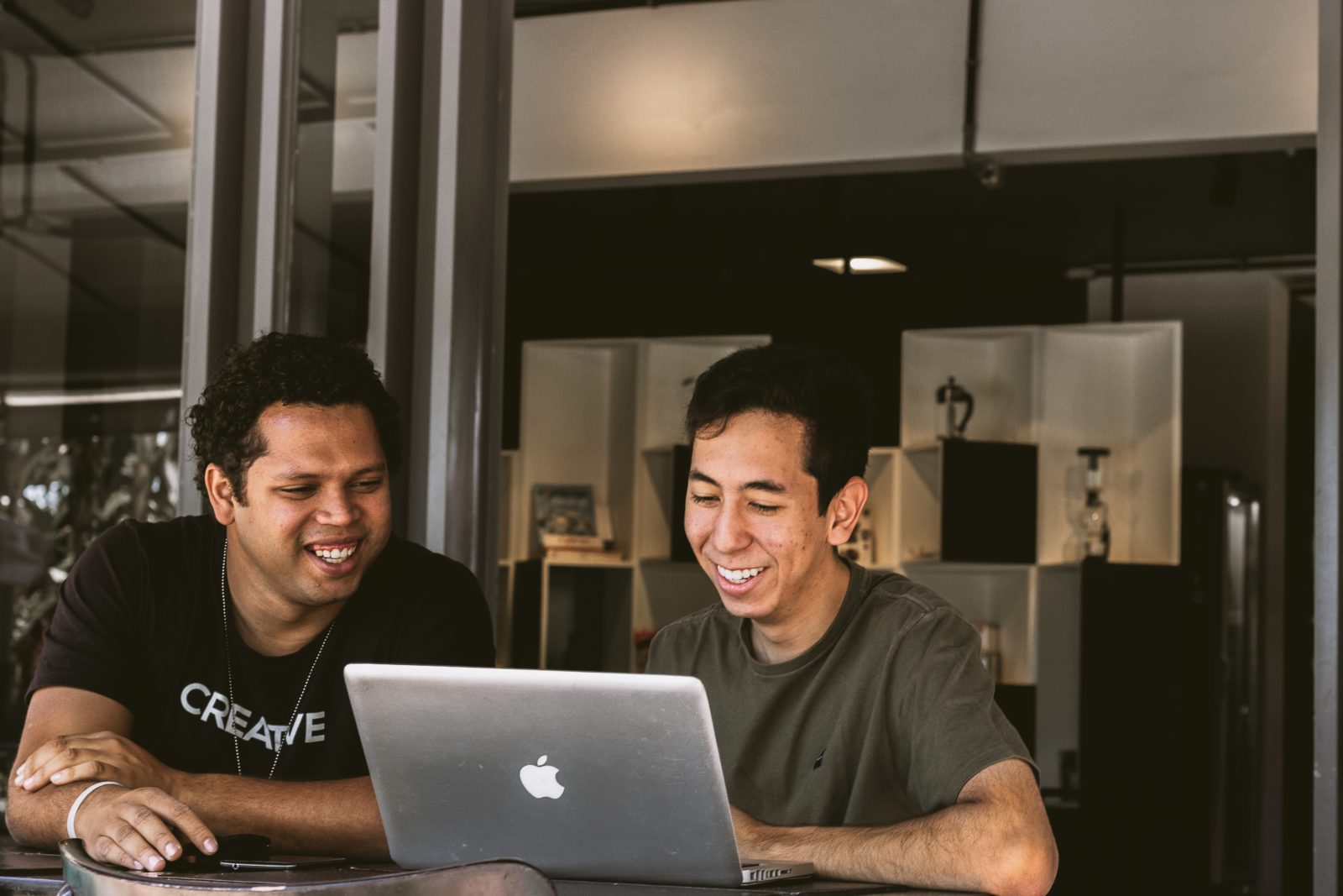 In this image, two smiling, relaxed men work together on a Macbook
