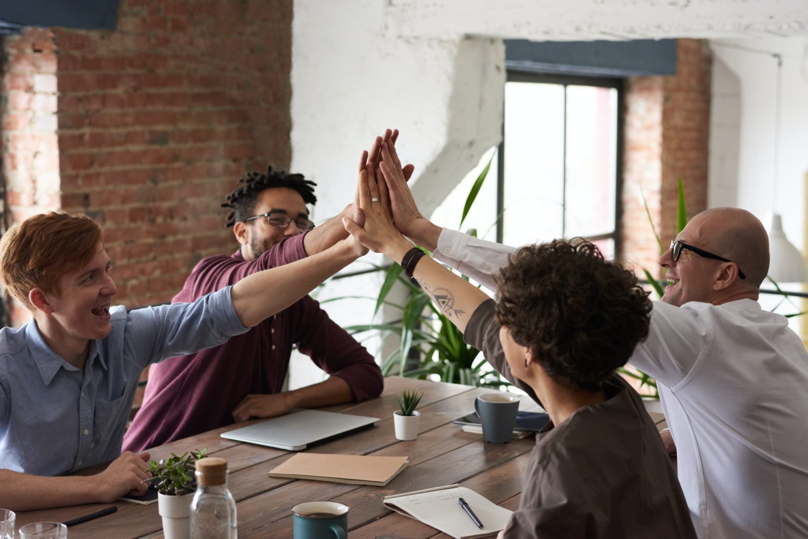 A team does a group high-five while sitting at a conference table in a contemporary office