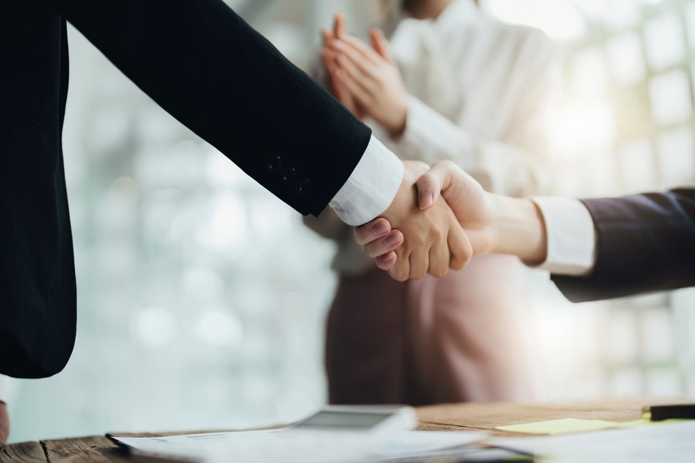 Major donor cultivation is a process that helps you build relationships with high-net-worth individuals who fund your organization. Two individuals shake hands while a third person looks on, clapping.