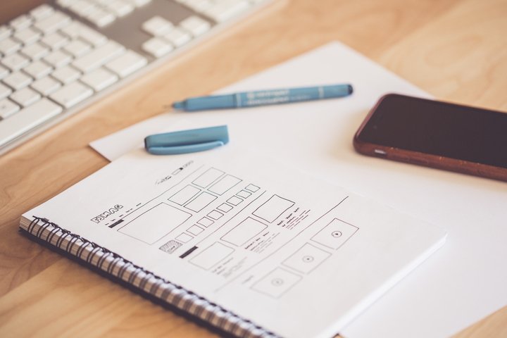 A notebook with a pen and phone sit next to a keyboard