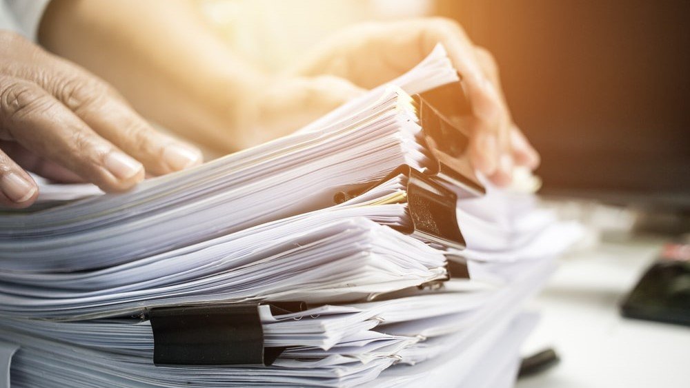 Manual approaches to donor account management will make your life much harder. Digital tools like a CRM can help. In this image, a person shuffles through a large stack of files.