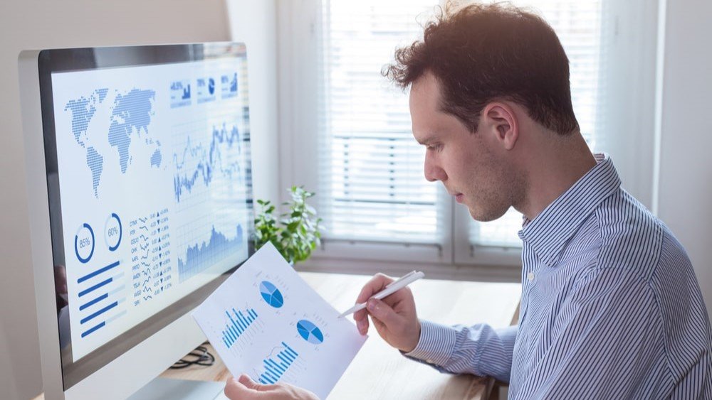 Fundraising KPIs will allow you to track your campaigns and improve your future results. In this image, a man sits in front of a computer, studying a chart.