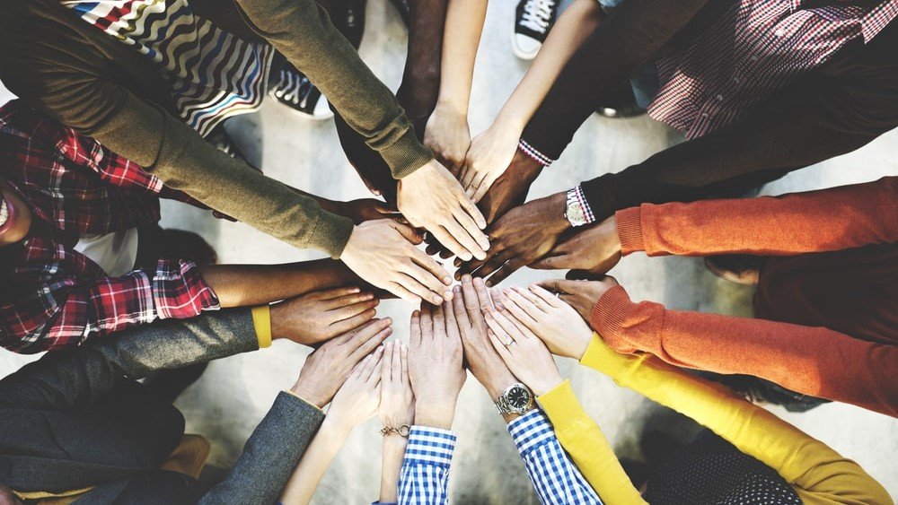 Nonprofit CRM integrations help you improve donor relationships. In this image, a group of people put their hands together to form a connected circle.