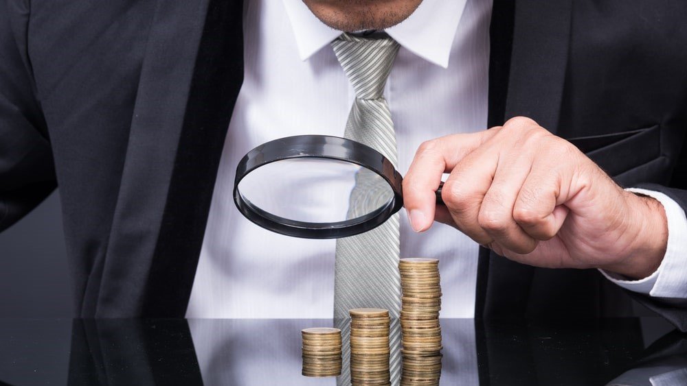 Effective nonprofit donation management helps you track the right donation details to drive engagement. In this image, a man in a suit examines three stacks of coins with a magnifying glass.