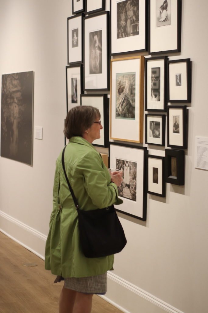 Woman in green jacket with black purse looks at photos on a museum wall.