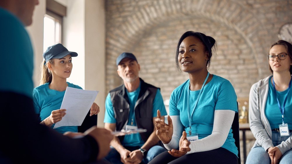 Growing nonprofits can benefit from a CRM as it allows them to manage many of the administrative tasks that waste resources like volunteer time. In this image, a group of volunteers sits together having a discussion.