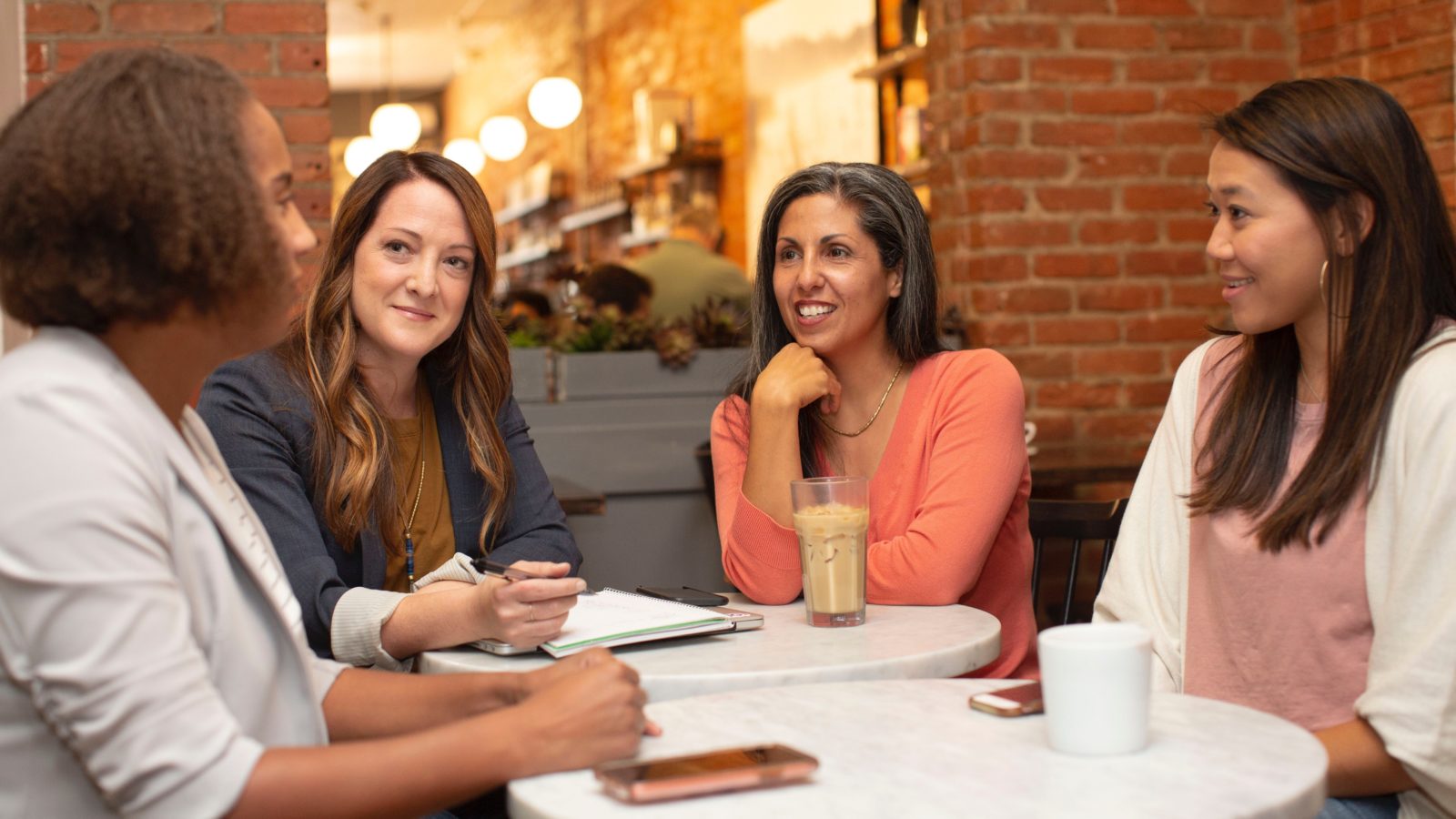 3 women sit in a restaurant listening to another woman tell them about her nonprofit's impact in the community. These kinds of in-person conversations are an important part of a winning donor management strategy.