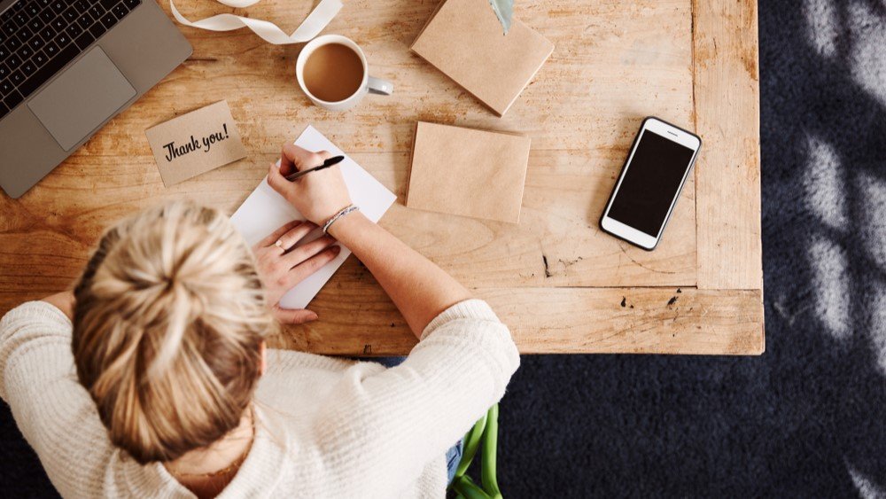 Donor recognition strategies can be as simple as sending personalized thank-you notes. In this message, a person writes a thank you note while sitting at a desk.