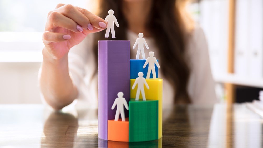 Nonprofit database segmentation can help you get to know your donors. In this image, a woman stacks figures onto a tiered set of colored blocks.