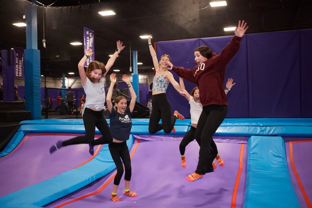 Five girls at a trampoline park in mid-jump, enjoying an outing from the Pickles Group.