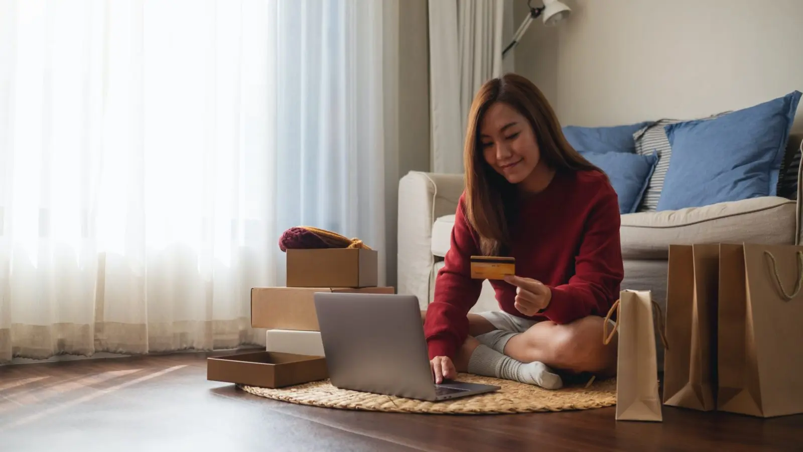 A woman sits cross-legged on the floor of her apartment typing a credit card donation to her favorite local nonprofit into her laptop.