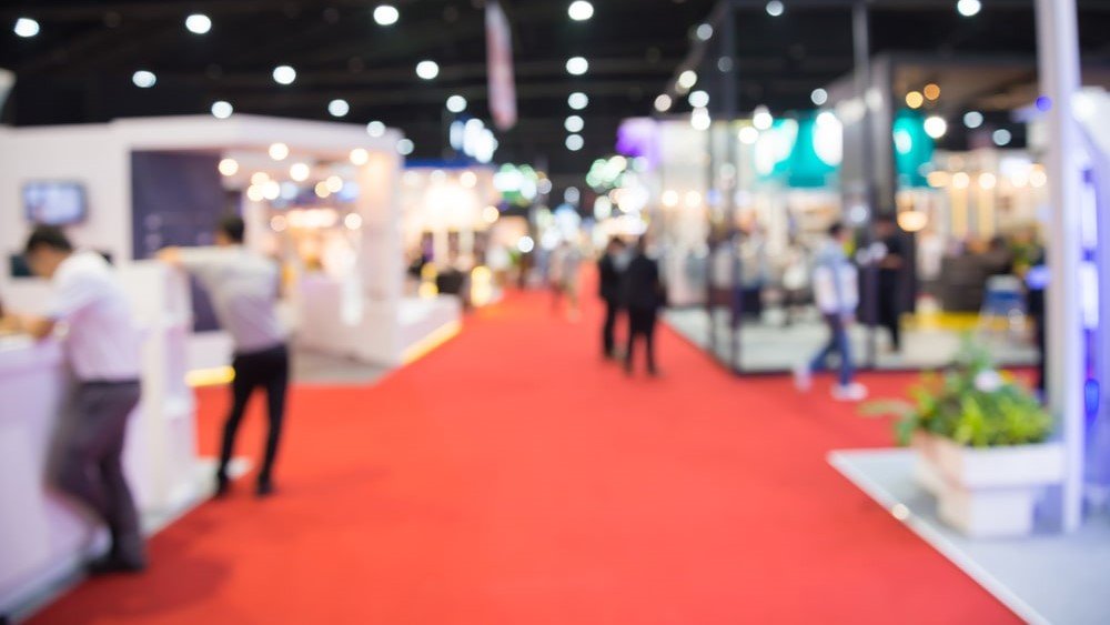 Association management software can help you streamline event management, like trade shows and conferences. In this image, individuals attend a conference in an out-of-focus shot.