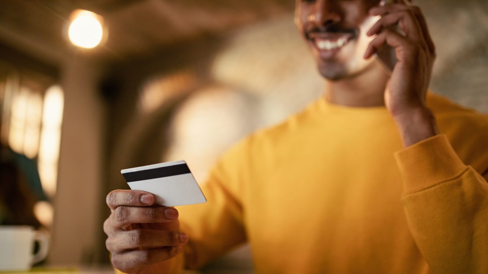 A smiling man in a yellow sweater looks at his credit card as he pays his membership dues over the phone.