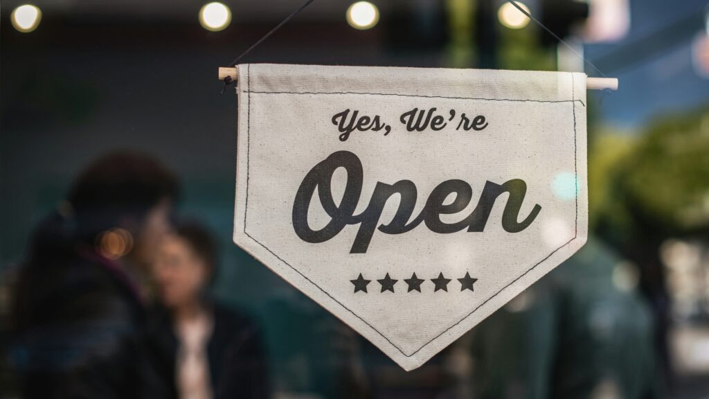 A sign hanging in a shop window that says yes we're open.